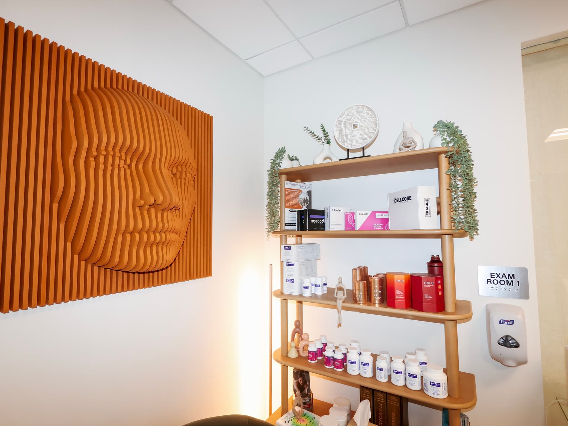 An exam room at Evolve Longevity with a wood-relief wall sculpture and shelves of supplements.