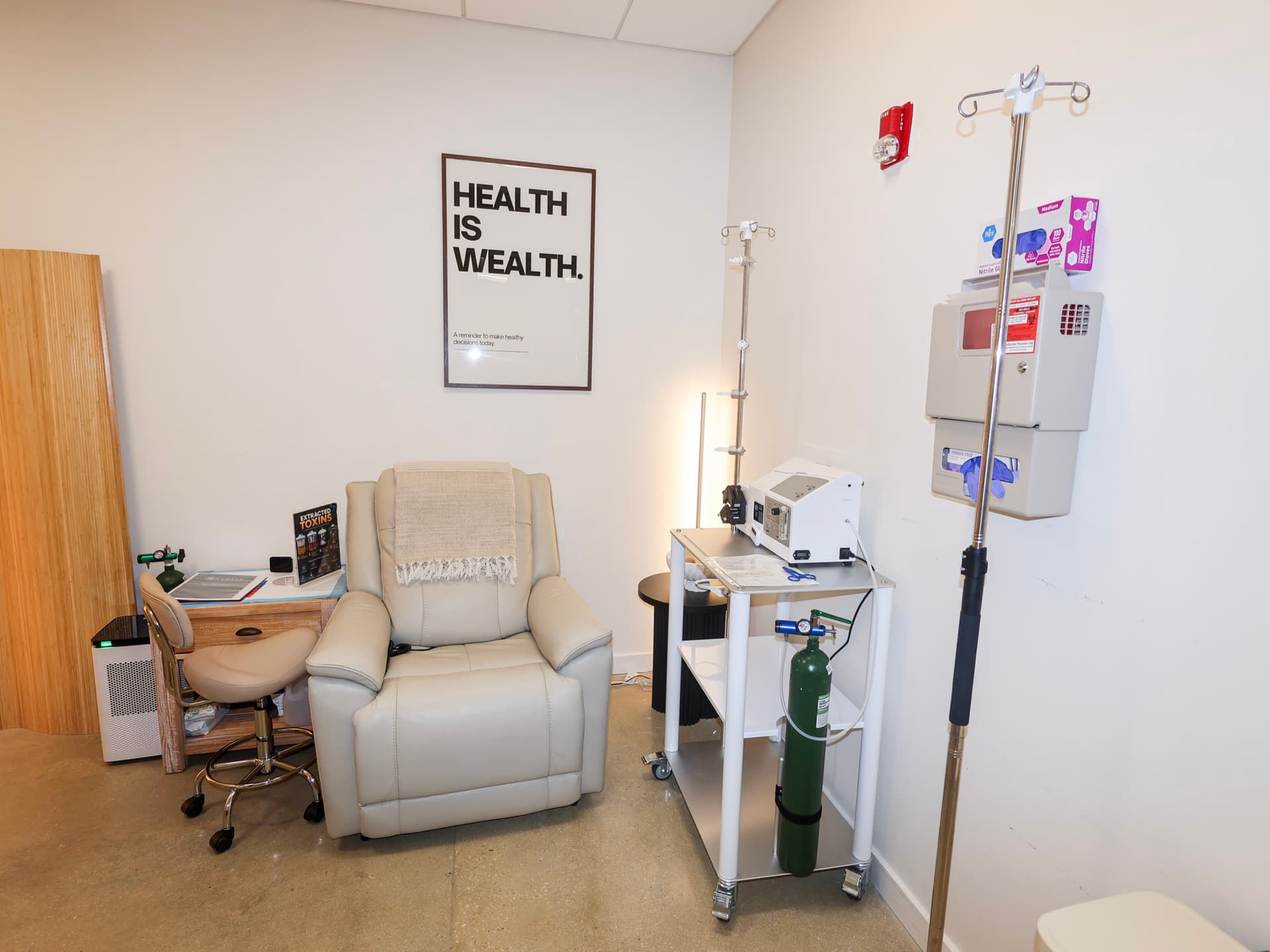 An infusion room at Evolve Longevity with a recliner, an IV pole, and a Health Is Wealth print.