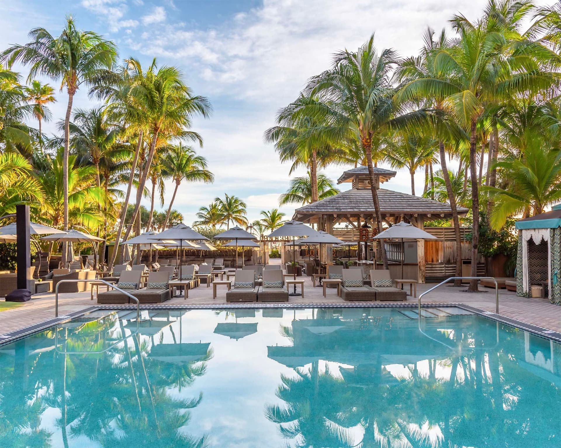 The palm-lined pool deck and thatched bar pavilion at The National Hotel Miami Beach