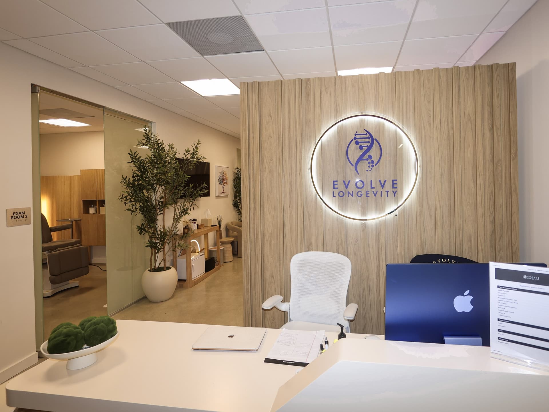 The reception desk at Evolve Longevity in Miami Beach, with a backlit clinic logo on a wood-slat wall.