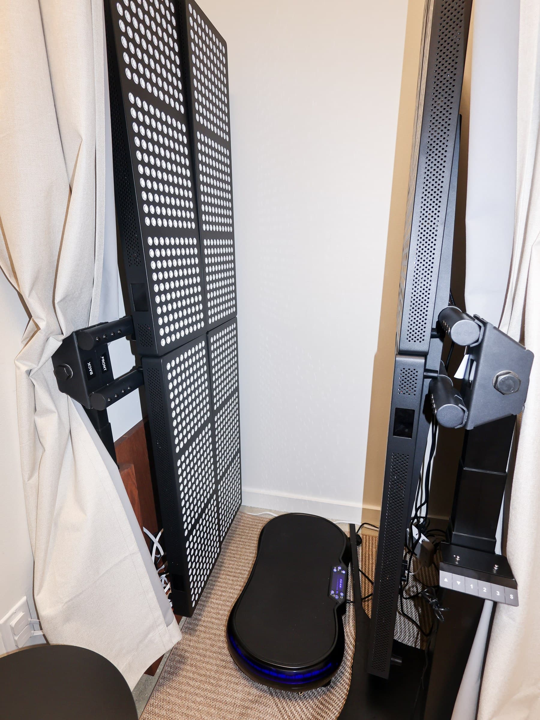 A red light therapy panel and vibration plate in a curtained bay at Evolve Longevity in Miami Beach.