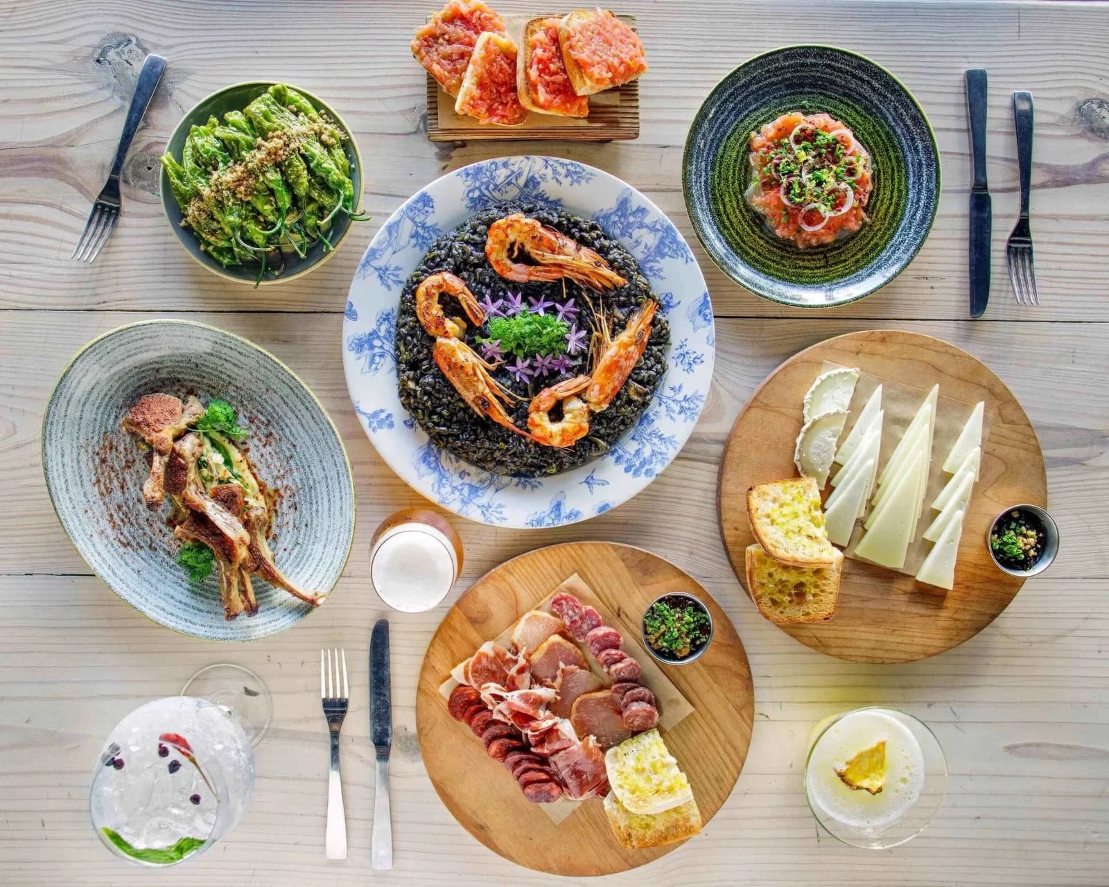 An overhead tapas spread with squid-ink rice, prawns, cheese, and cured meats at Barceloneta
