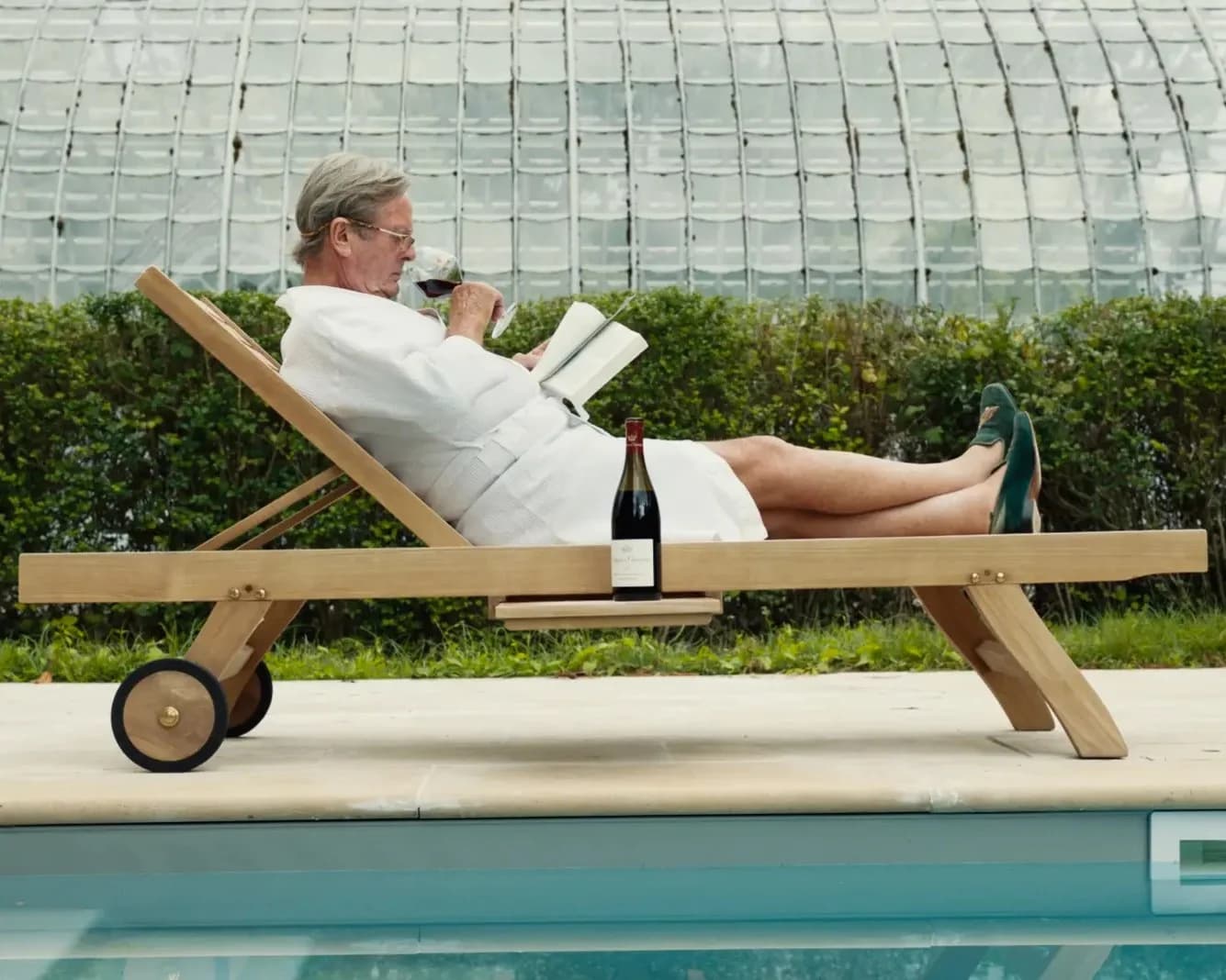 A man in a white robe reclines poolside with a glass and a bottle of red wine in a still from the documentary Burgundy